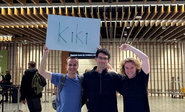 Three smiling men holding a sign that says 'Kiki' in an airport terminal.
