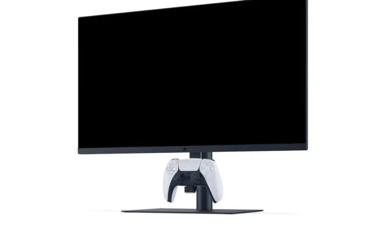 A white PlayStation 5 DualSense controller rests on the stand of a black monitor.
