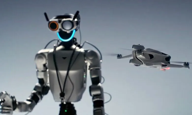 A humanoid robot with glowing blue mouth and orange-rimmed eyes stands next to a flying drone.