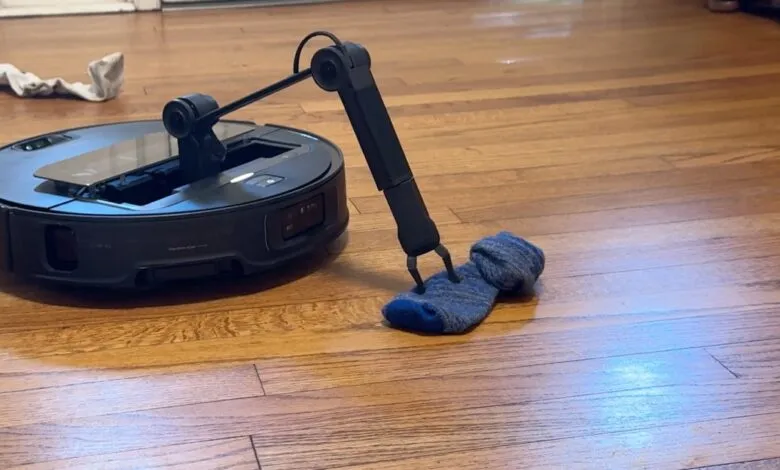 Roborock robot vacuum with robotic arm picking up a blue sock on hardwood floor.