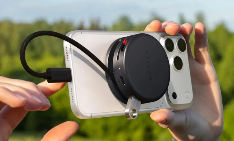 Hands holding an iPhone with a Satechi accessory attached, connected by a black cable.