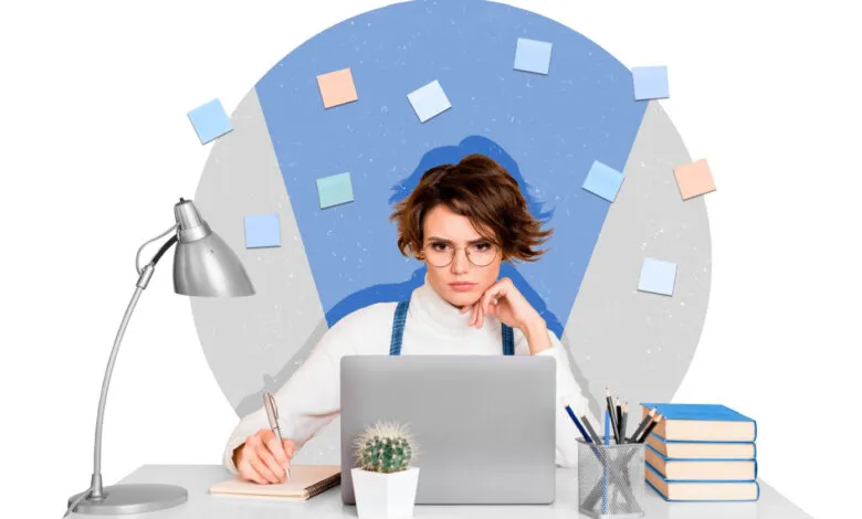 Woman with glasses at desk, laptop, notebook, lamp, and sticky notes.