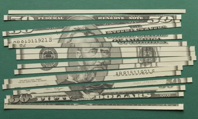 Close-up of a shredded US fifty-dollar bill on a green background.