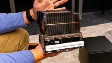 Hands hold a complex computer component with heatsink and ports.