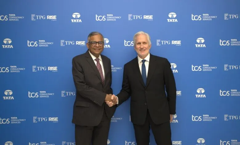 Two businessmen shake hands in front of a blue backdrop with company logos.