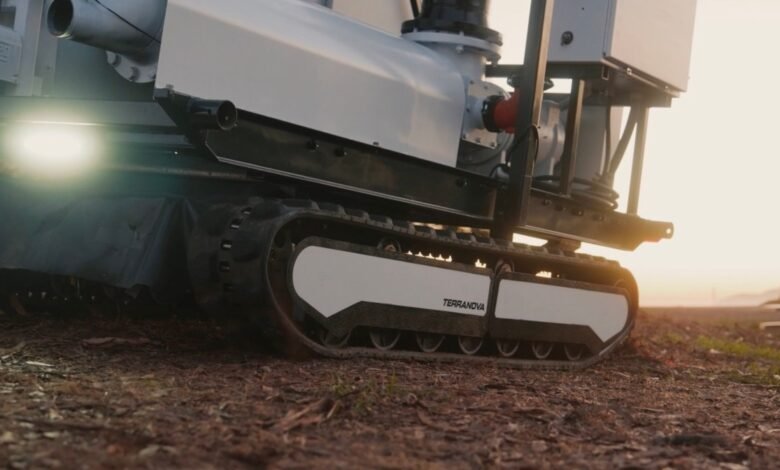 Close-up of a white tracked vehicle with the name TERRANOVA on its side, in a field at sunset.