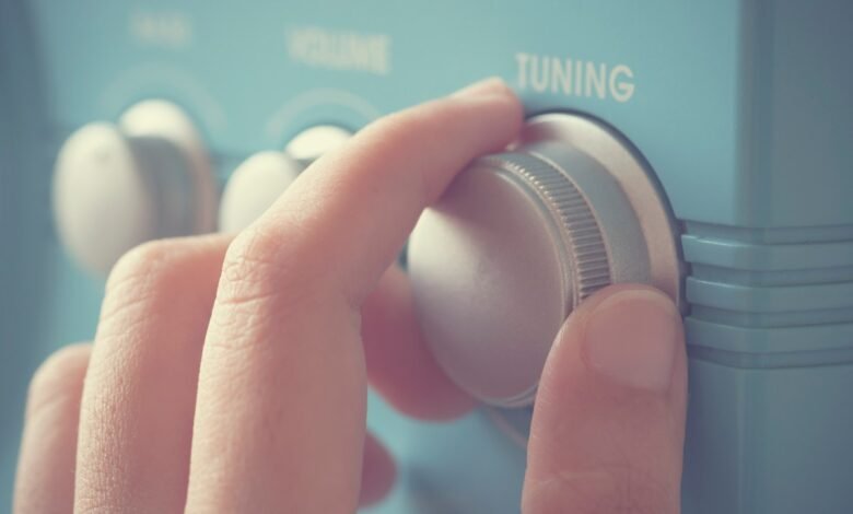 Close-up of a hand turning the tuning knob on a vintage blue radio.