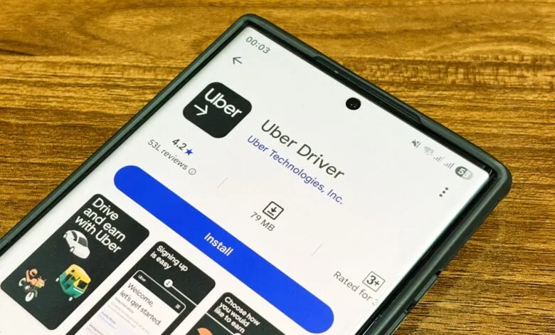 Close-up of a smartphone displaying the Uber Driver app page on a wooden surface.
