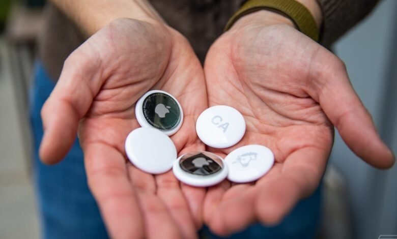 Hands holding multiple white Apple AirTags with visible logos and designs.