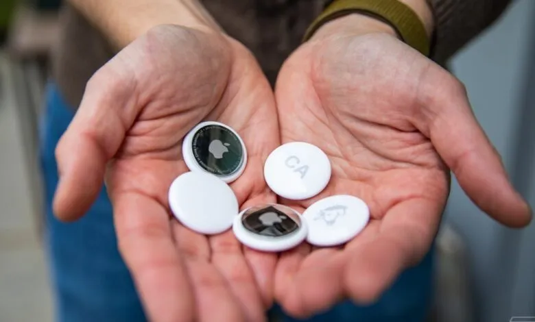 Hands holding multiple white Apple AirTags with visible logos and designs.
