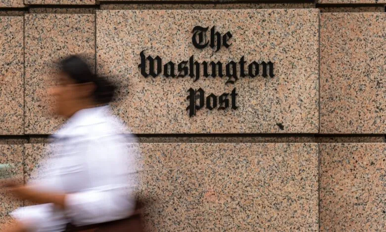 The Washington Post logo on a granite building facade with a blurred person walking by.