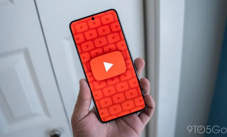 A hand holds a smartphone displaying the YouTube app interface with its iconic red play button.