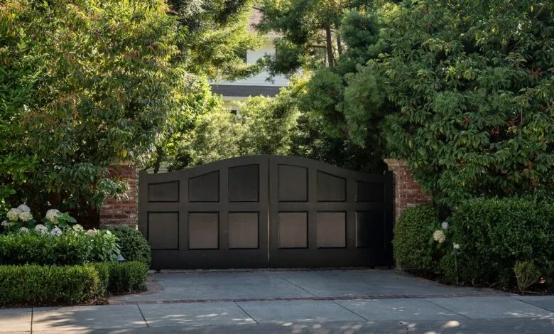 Large, dark, arched double gates flanked by lush greenery and brick pillars.
