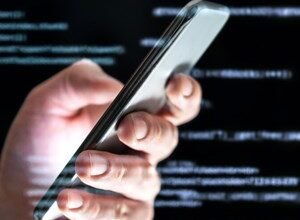 Hand holding a smartphone against a blurred background of computer code.