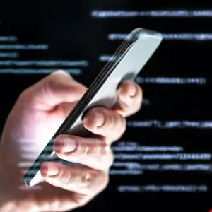Hand holding a smartphone against a blurred background of computer code.