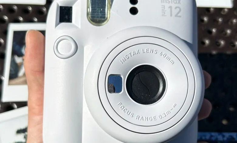 Close-up of a white Fujifilm Instax Mini 12 camera held in a hand.