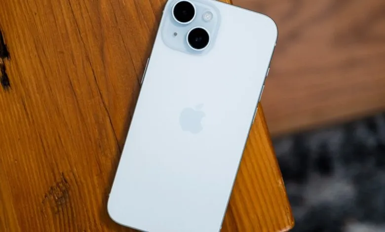 Back of a light blue iPhone with dual cameras on a wooden surface.