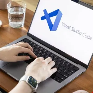 Hands typing on a laptop displaying Visual Studio Code logo and interface.