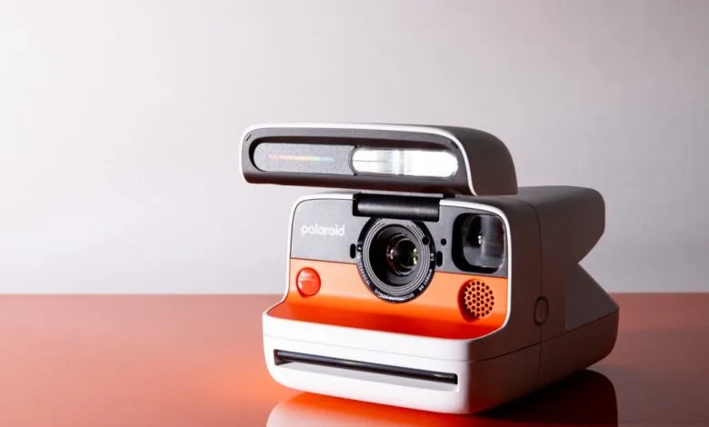 Polaroid camera with orange and white design, flash extended.