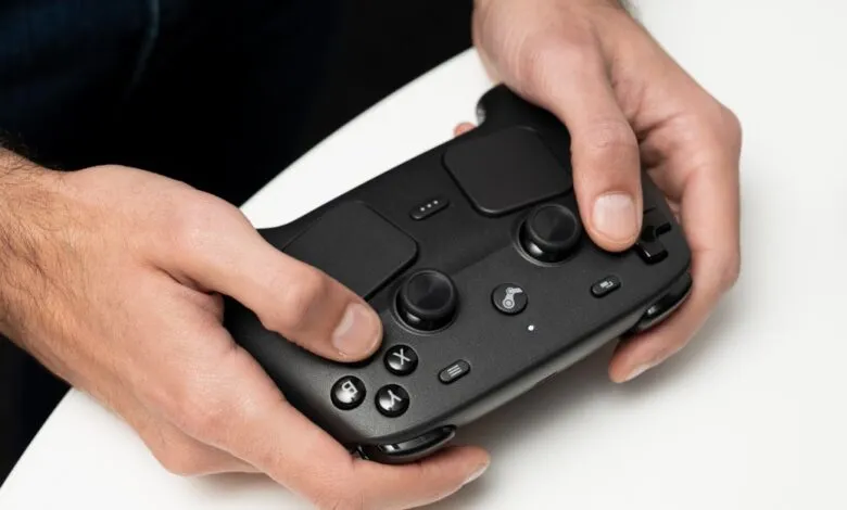 Hands holding a black Steam Deck controller against a white surface.