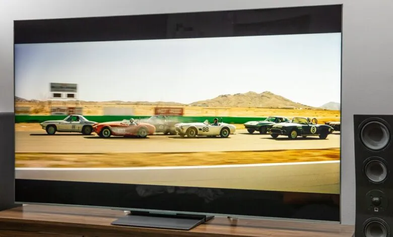 Large TV displaying vintage race cars on a wooden media console.