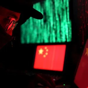 Person in glasses types on laptop with Chinese flag and green code on screens.