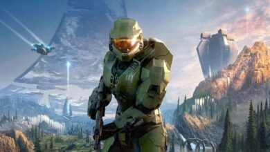 Master Chief stands ready in Halo Infinite landscape, with mountains and structures.