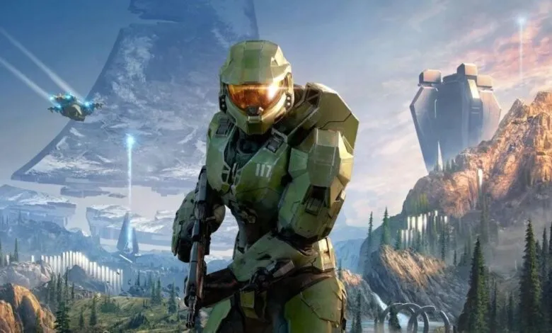 Master Chief stands ready in Halo Infinite landscape, with mountains and structures.