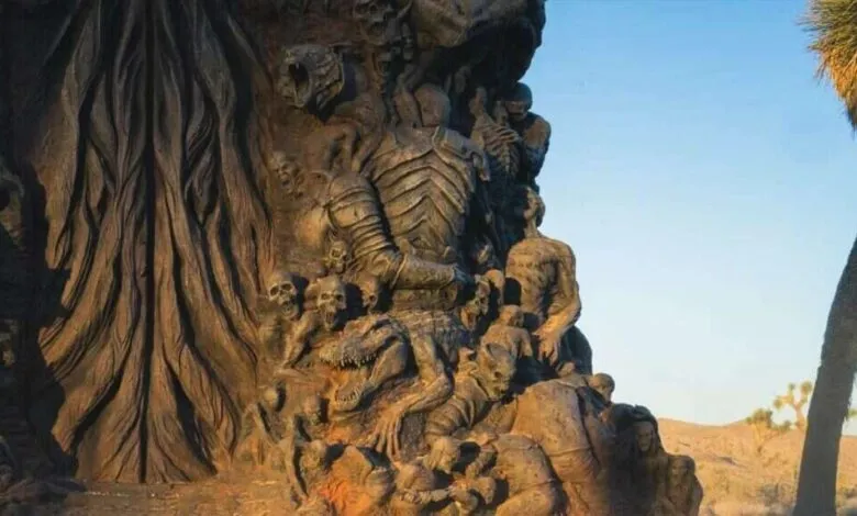 Detailed statue with figures, skulls, and an alligator-like creature in a desert landscape.