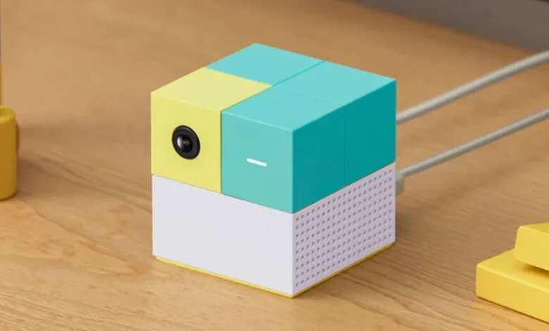 Colorful cube-shaped camera with yellow, teal, and white blocks on a wooden surface.