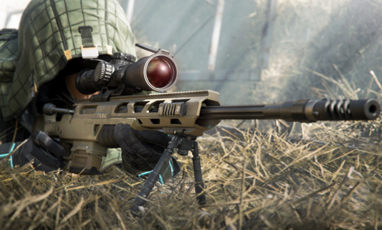 Camouflaged sniper with rifle and scope lying in tall grass.