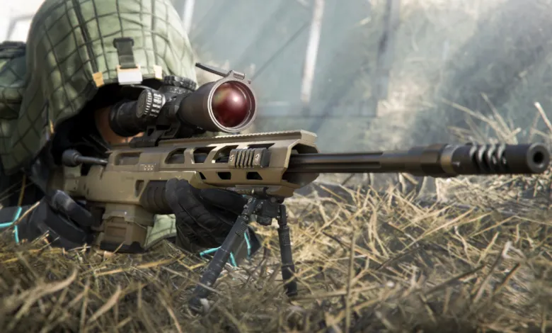 Camouflaged sniper with rifle and scope lying in tall grass.