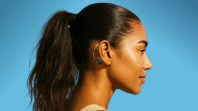 Profile of woman with dark hair in ponytail wearing ear patch against a bright blue background.