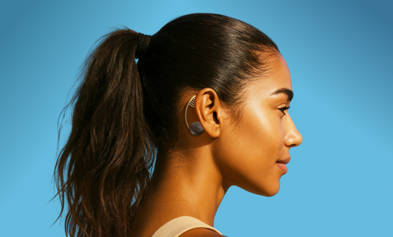 Profile of woman with dark hair in ponytail wearing ear patch against a bright blue background.