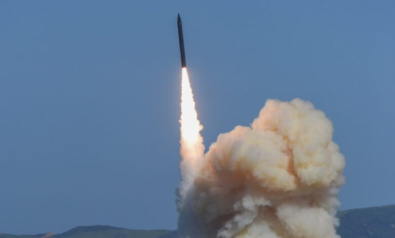 Missile launches with bright flames and smoke against a clear blue sky.