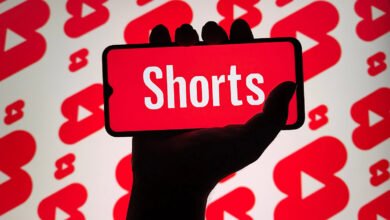 Hand holding smartphone displaying YouTube Shorts logo against YouTube play button background.