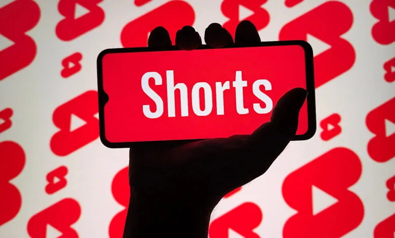 Hand holding smartphone displaying YouTube Shorts logo against YouTube play button background.