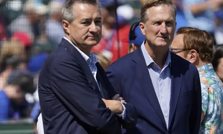 Two men in suits stand at a baseball game, looking serious.