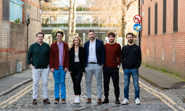 Six people stand in a row on a cobblestone street, posing for a photo.