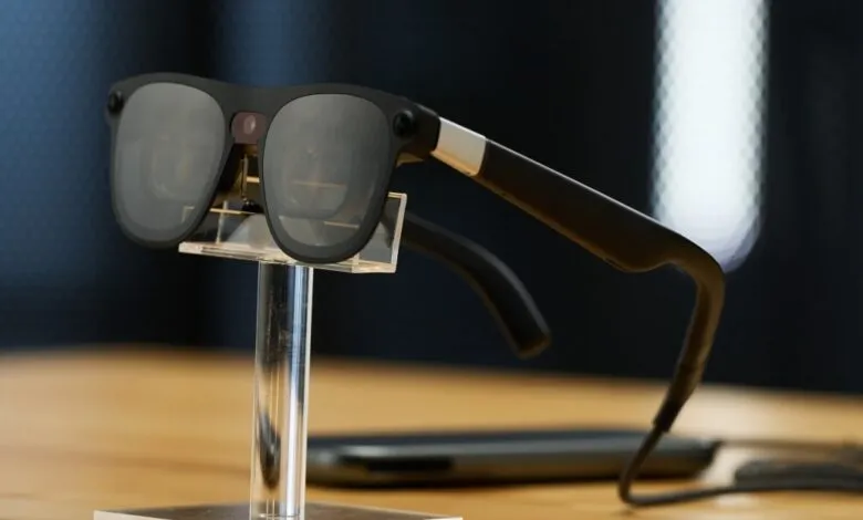 Smart glasses with dark lenses on a clear display stand.