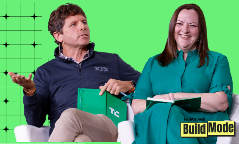 Two people sit on stage during a TechCrunch Build Mode event, smiling and talking.