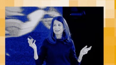 Woman presenting on stage, holding phone, gesturing with hands.