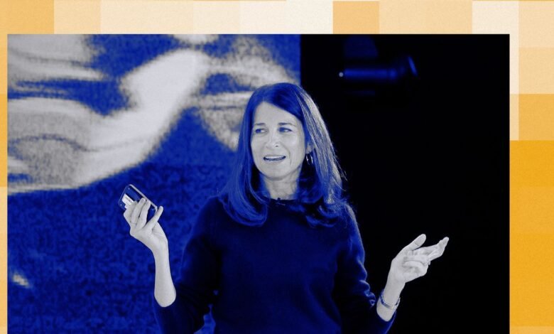 Woman presenting on stage, holding phone, gesturing with hands.