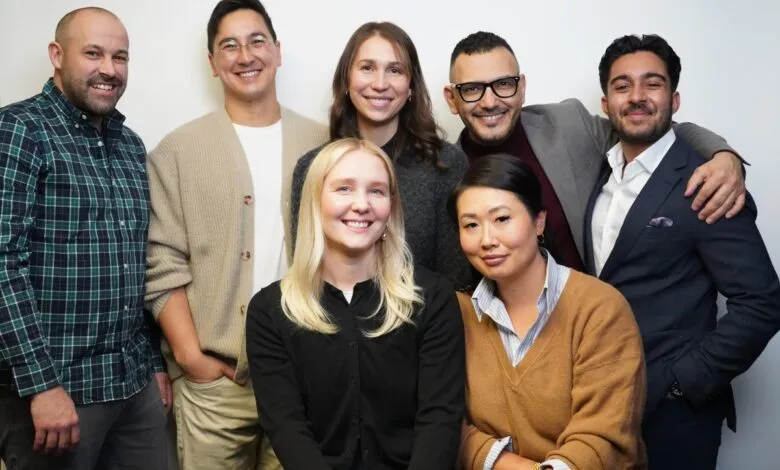 Group of seven diverse people smiling and posing against a white background.
