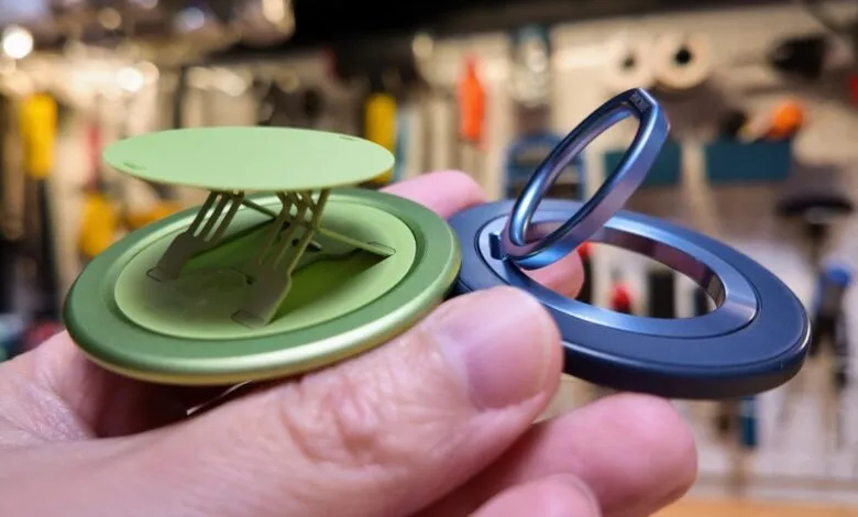 Hand holding green and blue phone grips with stands.