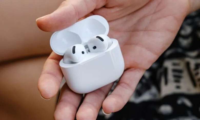 Hand holding open white AirPods Pro charging case with earbuds.
