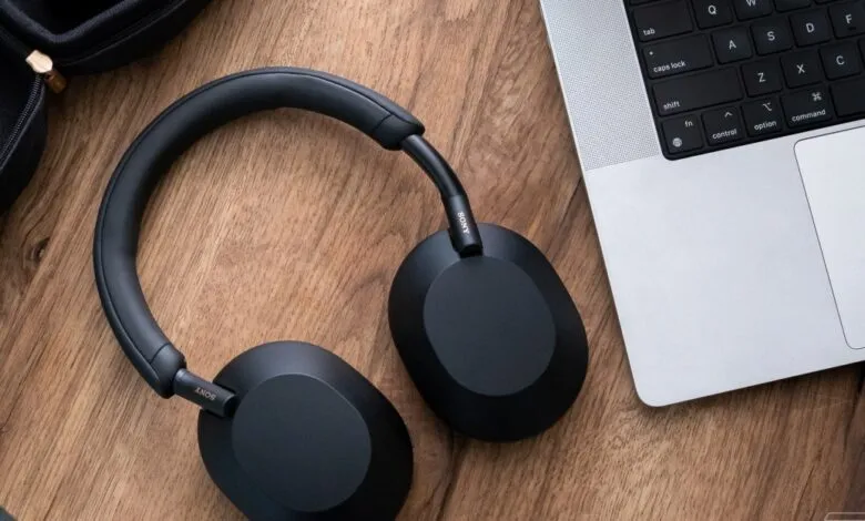 Black Sony headphones and a laptop sit on a wooden surface.