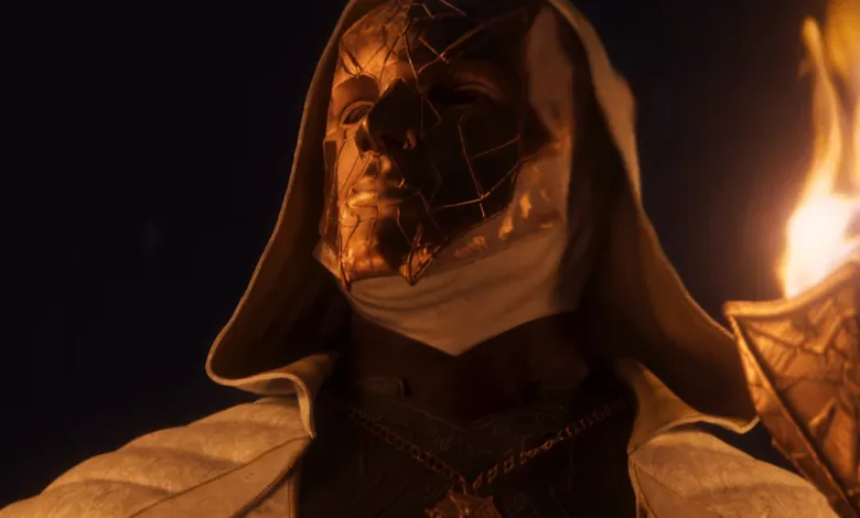 Person wearing golden mask and white robe, holding a torch.