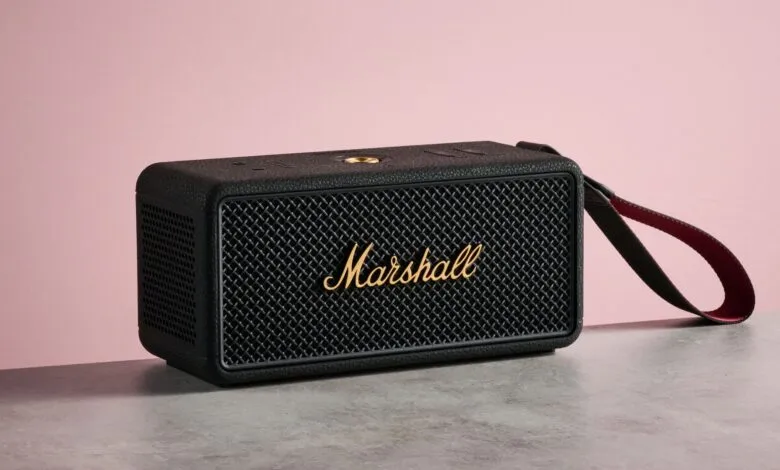 Black Marshall speaker with gold logo and red strap on gray surface.