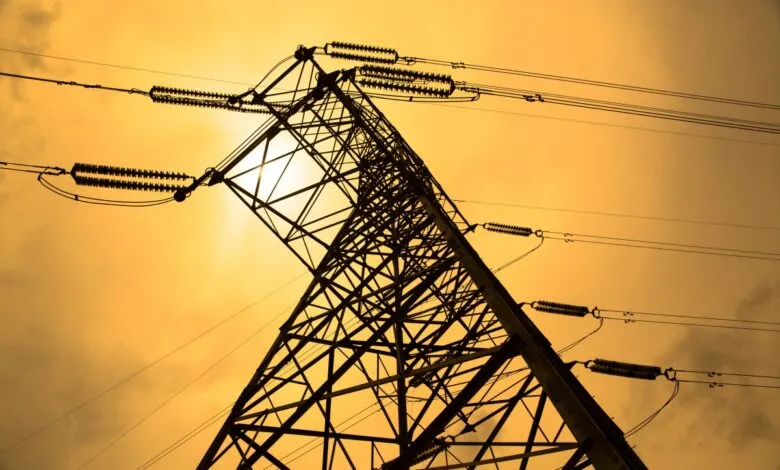 Silhouette of power line tower against a golden sky.